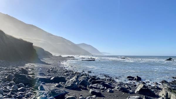 The morning sunlight starts to illuminate the rock-covered beach