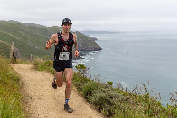 Chris smiles as he runs on coastal singletrack