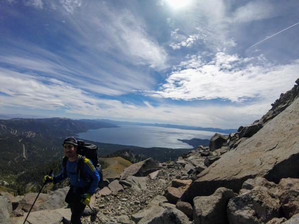 Chris hikes along a rocky mountainside, with Lake Tahoe in the background