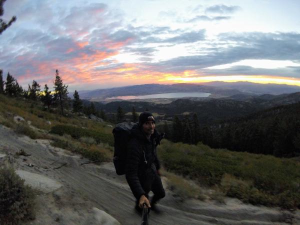 Chris on a mountainside trail, below a colorful sunrise